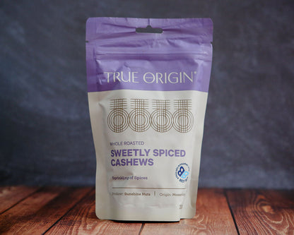 Bag of True Origin sweetly spiced cashews on a wooden surface with a dark background