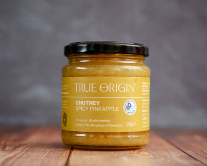 Jar of True Origin Spicy Pineapple Chutney on a wooden surface with a blurred background