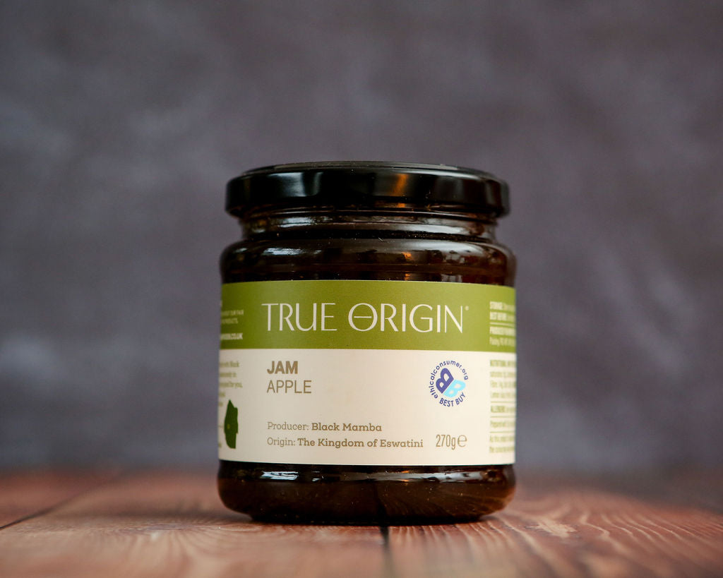 Jar of True Origin Apple Jam on a wooden surface with a blurred background