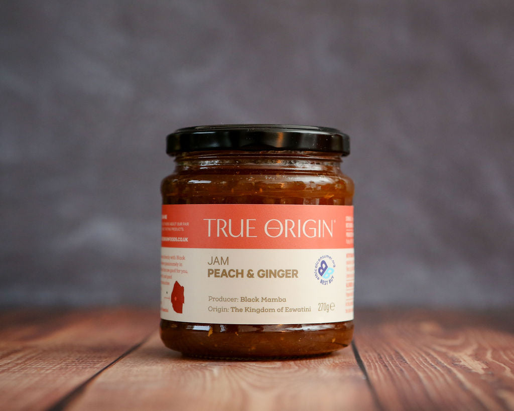 Jar of True Origin Peach & Ginger Jam on a wooden surface with a blurred background