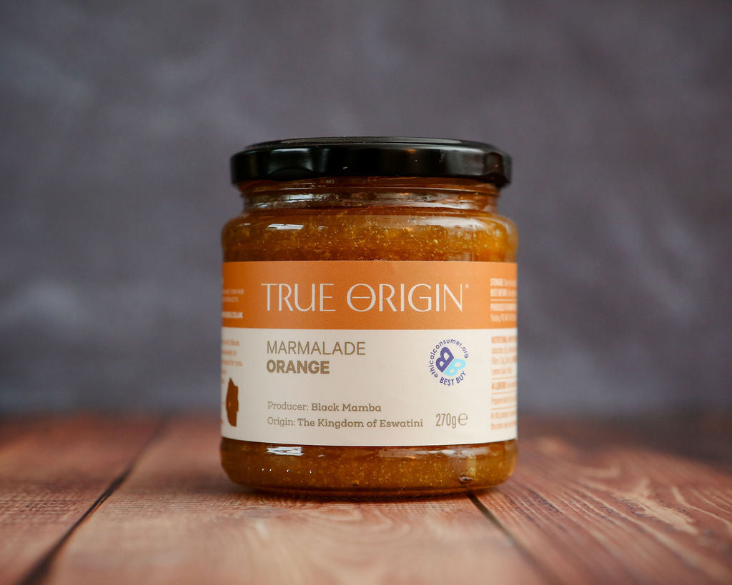 Jar of True Origin orange marmalade on a wooden surface with a blurred background