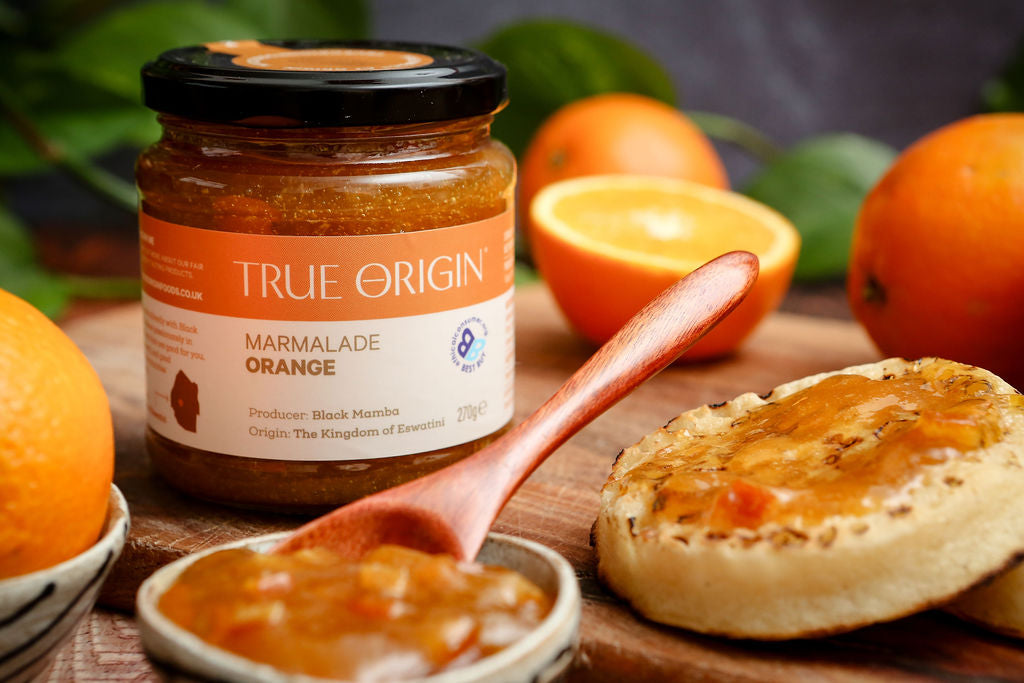 Jar of True Origin marmalade on a wooden board with crumpets and oranges