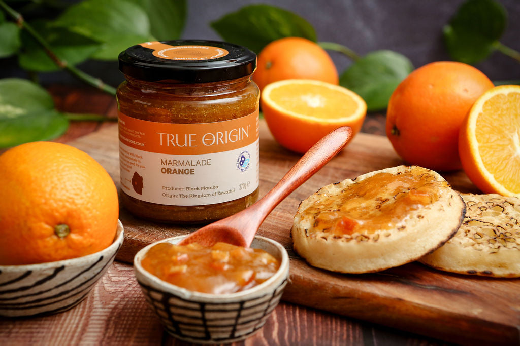 Jar of True Origin marmalade on a wooden board with crumpets and oranges