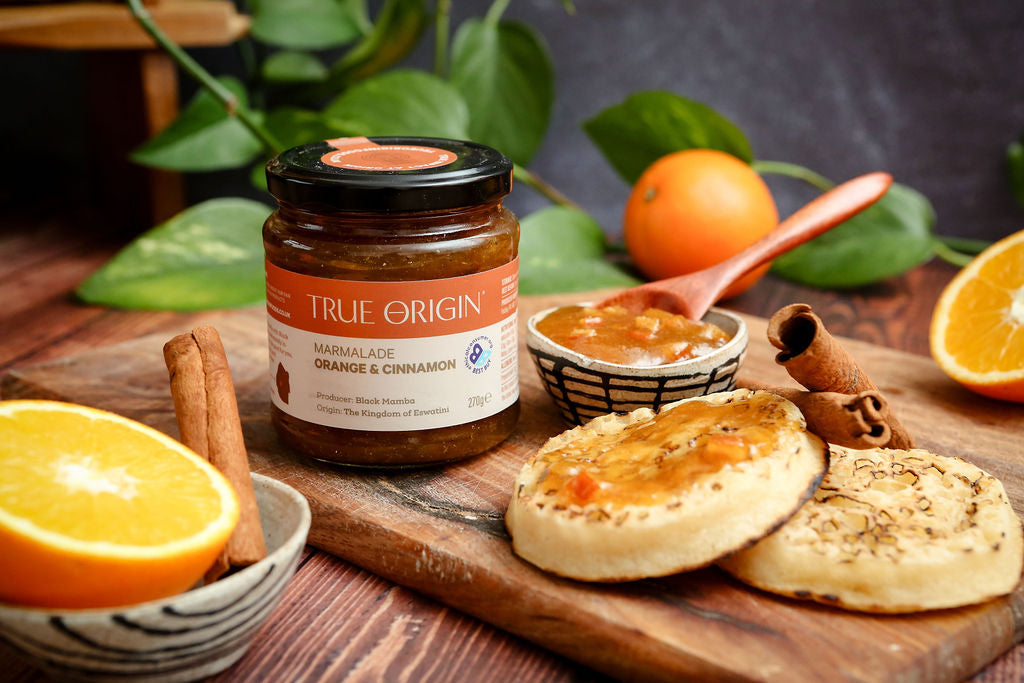Jar of True Origin marmalade on a wooden board with crumpets, oranges and cinnamon.
