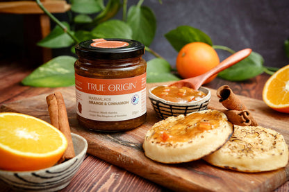 Jar of True Origin marmalade on a wooden board with crumpets, oranges and cinnamon.