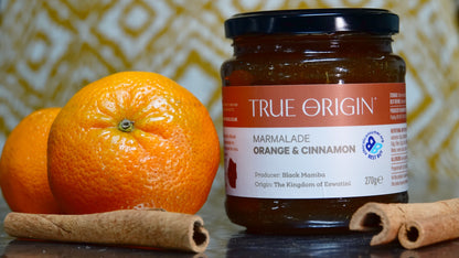 Jar of True Origin marmalade with oranges and cinnamon sticks on a textured surface
