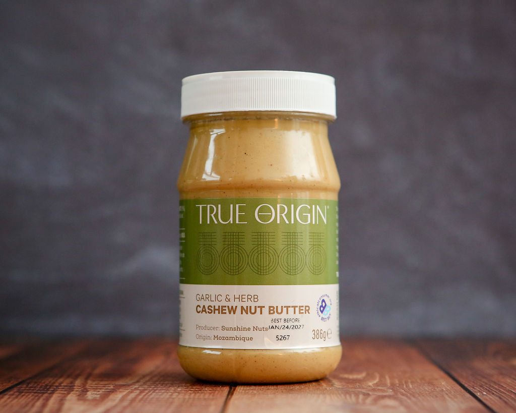 Jar of True Origin garlic & herb cashew nut butter on a wooden surface with a dark background