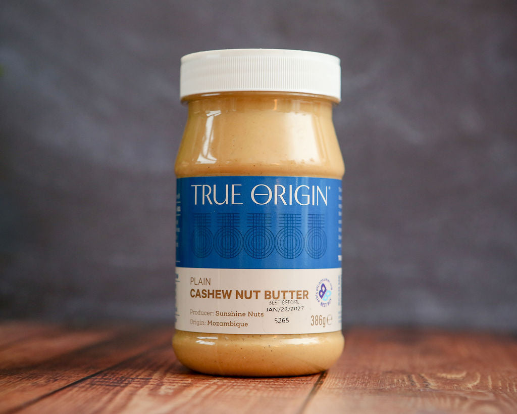 Jar of True Origin cashew nut butter on a wooden surface with a blurred background
