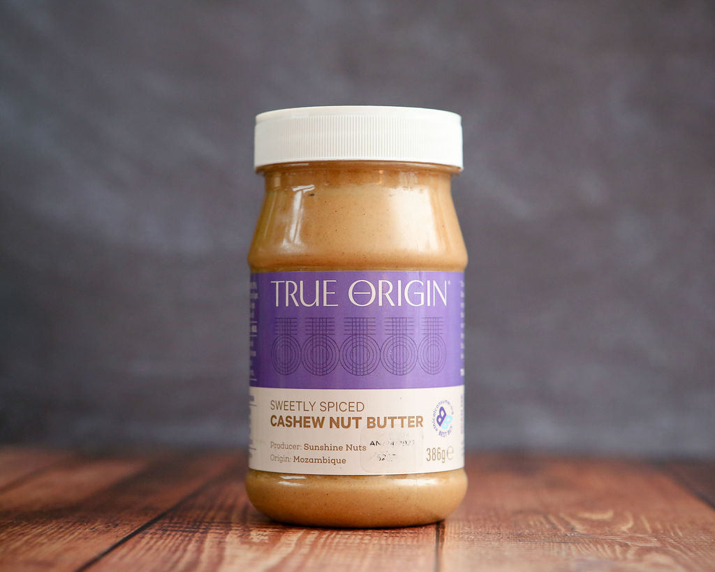 Jar of True Origin cashew nut butter on a wooden surface with a gray background