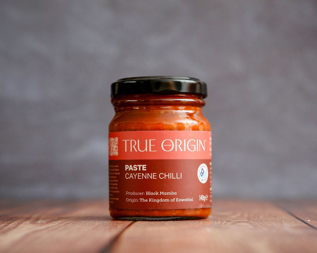 Jar of True Origin Cayenne Chilli Paste on a wooden surface with a gray background