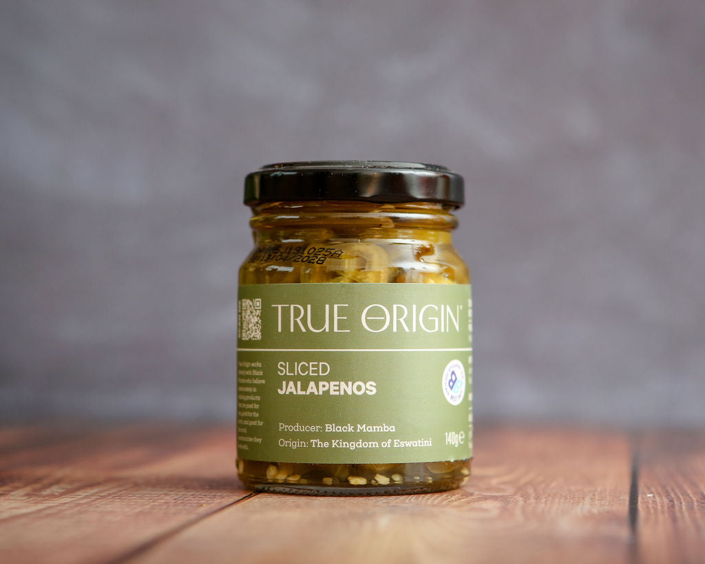 Jar of sliced jalapenos with 'True Origin' label on a wooden surface