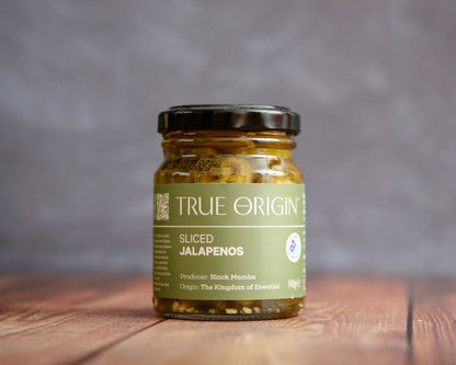 Jar of sliced jalapenos with 'True Origin' label on a wooden surface
